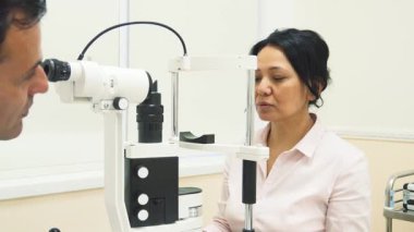 Genç bir kadın, parlak ve steril bir ofisteki sofistike bir göz inceleme cihazına başını yaslayarak öne doğru eğiyor. Özenli göz doktoru, görme sağlığının öncelikli olduğundan emin olmak için kapsamlı bir göz değerlendirmesi yapmaya hazır.