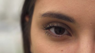 Çekici, genç, esmer bir kadın uzun kirpiklerini ve neşeli bir ifadeyle nazikçe gözlerini açıyor. Makro yakın plan, göz kapağının karmaşık detaylarını ve gözlerindeki ışıltıyı yakalar.