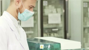 Kamera beyaz önlüklü genç bir laboratuvar teknisyenini test sonuçlarını dikkatle incelerken yakalıyor. Lateks eldivenlerle, bulguları titizlikle sarı bir klasöre kaydediyor, bilimsel keşfe olan bağlılığını gösteriyor.