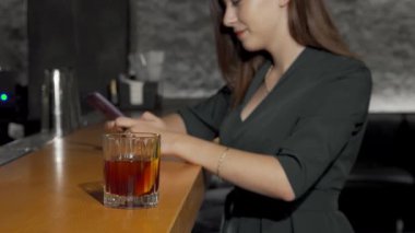 Şık giyinmiş şık bir kadın barın üzerine eğiliyor, akıllı telefonuyla güzel bir kokteyl hazırlıyor. İçkinin sıcaklığı, şık bar dekoruyla çelişiyor. Bu da davetkar bir atmosfer yaratıyor.