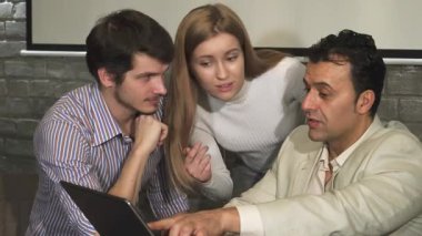 Değişik profesyonellerden oluşan bir grup, yenilikçi fikirler üretirken bir dizüstü bilgisayara odaklanmış canlı bir tartışmaya girişiyor. Atmosfer yaratıcılık ve takım çalışmasıyla doludur, modern bir ofiste farklı bakış açılarının sinerjisini gösterir.