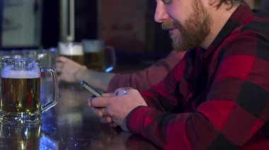 Tarz sahibi, genç, beyaz sakallı bir adam şık bir barda otururken akıllı telefonuna derinden odaklanır. Bar ışıklarının sıcacık parıltısı ekose gömleğinden yansıyor, yazarken rahat bir atmosfer yaratıyor, anın tadını çıkarıyor.