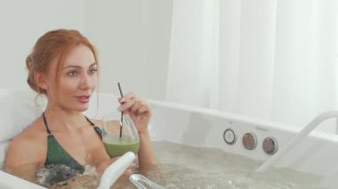 Zarif bir kadın lüks bir girdap banyosunda dinlenir, pipetle ferahlatıcı yeşil bir smoothie yudumlar. Yumuşak ışıklandırma ve kaynayan suyla güçlendirilmiş sakin atmosfer, nihai spa deneyimini somutlaştırıyor, sağIığı ve sükuneti teşvik ediyor.