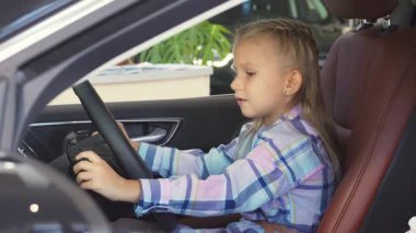 Sarı saçlı sevimli küçük bir kız direksiyonda güvenle oturur, parlak bir gülümsemeyle anahtarlara uzanır. Canlı mor elbisesi ve şakacı tavırları davetkar bir atmosfer yaratıyor. Arkasındaki macera heyecanını gözler önüne seriyor.