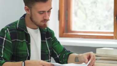 Siyah saçlı ve bakımlı sakallı ciddi bir genç adam parlak bir sınıftaki bir kitabın sayfalarını dikkatle inceliyor. Etrafında edebiyat yığınları ve sıcak bir pencere ışığı ile kendini adamış ve bilginin peşinde koşuyor.