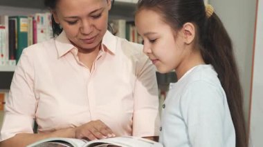 Olgun bir Asyalı kadın ve büyüleyici kızının kütüphanede enfes bir kitap seçimiyle meşgul olduğu iç açıcı bir sahne. Paylaştıkları gülücükler ve odaklanmış ifadeleri öğrenme sevincini ve keşfettikleri gibi ailenin özel bağını vurgular.