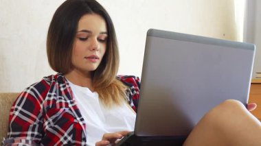 Genç bir kadın, yumuşak ışıklı odasındaki rahat bir kanepede, bilgisayarında canlı bir görüntülü sohbete dalmış olarak rahatça oturuyor. Sıcak bir gülümseme ile, neşeli bir şekilde arkadaşına bir öpücük yolluyor, neşe ve bağlantı yayıyor.