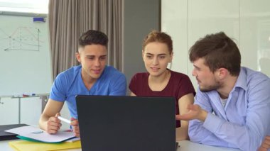 Gösterişli bir ofis alanında, üç genç profesyonel bir dizüstü bilgisayarın etrafında canlı bir tartışmaya girişiyor. Yakışıklı esmer adam ekranda bir kalemle işaret ederken, güzel kızıl saçlı kadın dikkatle dinliyor, iki şık beyaz adam tarafından çevrelenmiş.