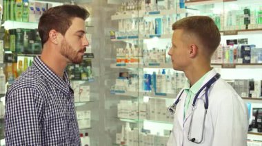 Gıcır gıcır bir tıbbi elbise giymiş odaklanmış bir doktor, renkli ilaç ürünleriyle çevrili bir hastayla düşünceli bir sohbete girişir. Atmosfer profesyonel ama davetkar, sağlık hizmetlerinin önemini vurguluyor ve