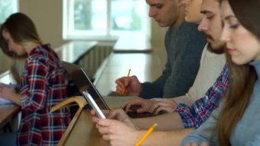 Kafkas öğrencilerden oluşan çeşitli bir grup, iyi aydınlatılmış bir kolej konferans salonunda, derslerine derinden odaklanmışlar. Kenar görünümü, bazıları dizüstü bilgisayar kullanarak, bazıları da kalemle notlar yazarak farklı not alma yöntemlerini yakalar.