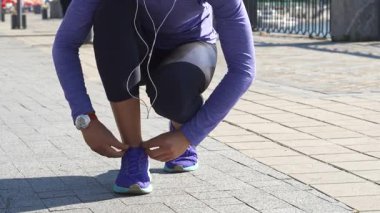 Genç bir kadın, parlak mor spor ayakkabılarının bağcıklarını onarmak için güneşli bir nehir yolunda zarifçe çömeliyor. Odaklanmış bir ifadeyle, kilosunu değiştiriyor, açık hava macerası için ayakkabılarını mükemmel bir şekilde bağlıyor.