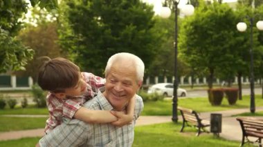 Neşeli, kıdemli bir adam neşeli torununu sırtında taşırken neşeli bir parktaki yemyeşil çiçeklerle parıldıyor. Küçük çocuk, esmer saçlarıyla, neşeli bir şekilde ileriye bakıyor, macera ve aşkın ruhunu somutlaştırıyor.