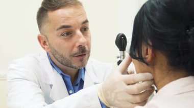 Kendini işine adamış doktor hastaların gözlerini titizlikle incelemek için özel bir cihaz kullanarak yaklaştı. Sıcak gülüşü ve nazik tavırları, bu önemli sağlık kontrolü sırasında hastayı rahatlatan güven verici bir atmosfer yaratıyor.