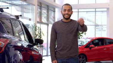 Şık bir Afrikalı Amerikalı adam, modern bir sergi salonunda yeni ve şık bir kesişen arabanın anahtarını tutarken gururla ışıldıyor. Bu canlı sahne bir araç satın almanın heyecanını yakalıyor, gururlu bir araba sahibi olmanın sevincini gösteriyor.