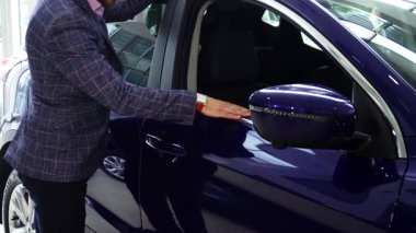 Genç bir satıcı, hayranlığını göstermek için, patlıcan renginde çarpıcı bir arabanın parlak yüzeyini nazikçe okşar. Hevesle kapıyı açar, konfor ve stil vaat eden lüks bir iç mekan sunar, her akıllı alıcı için mükemmeldir.