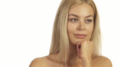 Göz kamaştırıcı sarışın bir kadın eli çenesinde duran el değmemiş beyaz bir duvara karşı düşünceli bir şekilde duruyor. O, sıcak bir gülümseme ile kameraya dönmeden önce çeşitli yönlere bakar, güzellik ve güven saçar.