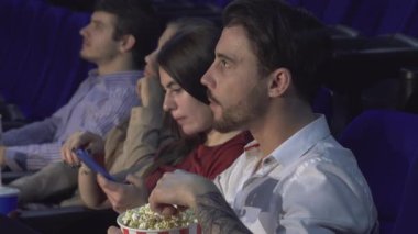 Canlı dört arkadaştan oluşan bir grup canlı bir sinema salonunda yan yana oturur, ekrandaki film karşısında büyülenir. Siyah saçlı genç adam patlamış mısır yerken, kız arkadaşı uzun siyah saçlı, cep telefonuna bakarken gülümsüyor.