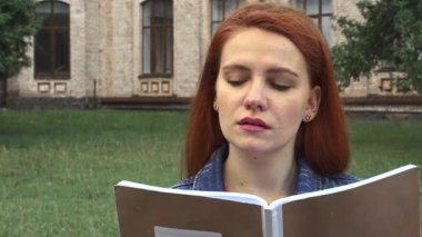 Neşeli kızıl saçlı bir öğrenci üniversitenin yakınındaki yemyeşil bir parkta kitabına dalmış, bakışları ışıl ışıl bir gülümsemeyle kameraya yükseliyor. Canlı yeşillik ve yumuşak esinti onun gençlik enerjisini ön plana çıkaran ferahlatıcı bir atmosfer yaratır.