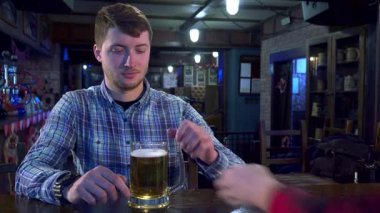 Çekici bir gülümsemesi olan neşeli genç bir adam barda buzlu bir bardak bira kaldırıyor. Çekici beyaz adam, şık bir damalı gömlek giymiş, barmenle bir dakikalık arkadaşlıktan zevk alıyor, hayat dolu...