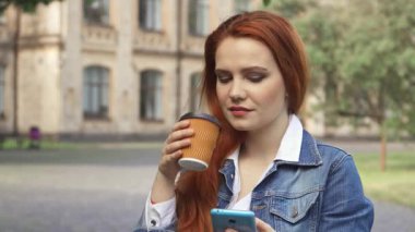 Çekici, kızıl saçlı beyaz bir kız öğrenci akıllı telefonuna dalmışken şık bir bardaktan kahve yudumluyor. Resmedilmeye değer bir kampüs zeminine kurulmuş neşeli ifadesi odak ve haz karışımı yayarak özünü yakalıyor.