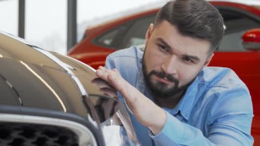 Bakımlı sakallı çekici bir adam galeride yeni bir arabayı yakından inceliyor, kendine güven ve heyecan saçıyor. Bu ilgi çekici sahne, modern tasarımın altını çizerek mükemmel otomobili seçmenin heyecanını yakalıyor.