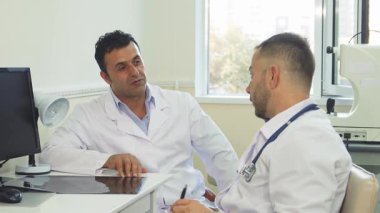 İki dost canlısı doktor, bir erkek ve bir kadın, parlak bir ofiste oturup, esprili bir değiş tokuş üzerine kahkahalar atıyorlar. Sıcak gülümsemeleri ve rahat tavırları, mesleklerindeki dostluk ve neşeyi gösteren davetkar bir atmosfer yaratıyor.