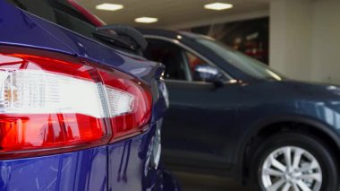 Şık mavi bir takım elbise giymiş seçkin bir araba satıcısı, hareketli bir motor fuarında lüks bir aracın yanında dururken anahtarlarını kendinden emin bir şekilde sergiliyor. Etrafındaki parıldayan arabalar potansiyel alıcıların heyecanını yansıtıyor.