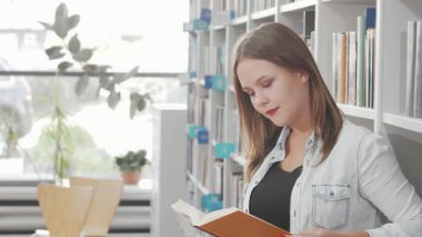 Sıcak bir gülümsemesi olan çekici genç bir kadın, rahat bir kütüphanede edebiyatla dolu raflarla çevrili bir kitapla boğuşuyor. Rahatlamış tavrı ve davetkar atmosferi mükemmel bir eğitim ve rahatlık karışımı yaratıyor.