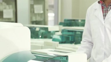 Dinamik bir laboratuvar ortamında, beyaz önlüklü genç bir laboratuvar teknisyeni renkli numunelerle dolu bir test tüpünü ustalıkla meslektaşına veriyor. Bu yakın çekim, bilimsel araştırmalarda takım çalışmasının ve hassasiyetin özünü yakalar.