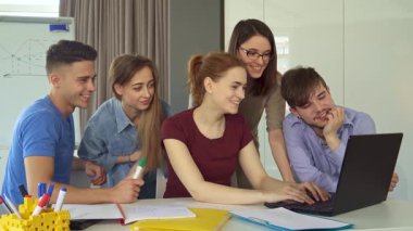 Genç beyaz profesyonellerden oluşan canlı bir ekip şık bir ofis çalışma alanında canlı bir işbirliği içinde. Dizüstü bilgisayarlar açık ve renkli kırtasiyelerle, üç çekici kadın ve iki yakışıklı erkek fikirlerini paylaşıyor, yaratıcılığı teşvik ediyor ve