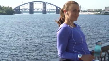 Dinamik bir sahne, genç ve çekici bir kadını nehir kenarında dinlenirken, müziğinin içinde kaybolurken parmaklıklara yaslanırken yakalar. Uzun, siyah saçları at kuyruğu ile bağlanmış ve canlı bir menekşe bluz giymişti, düşünceli bir şekilde dik dik bakıyordu.