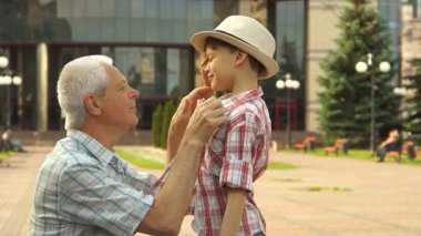 Neşeli bir son sınıf öğrencisi dışarıda torununa sevinçle sarılır, sıcaklık ve sevgi saçar. Çekici gri saçlı dede, ekose gömlek giyiyordu. Sevimli küçük oğluyla samimi bir anı paylaşmak için çömelmişti. Sevimli bir şekilde mutlulukla ışıldıyordu.