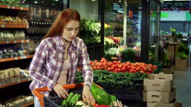 Canlı, genç, beyaz bir kadın hareketli bir süpermarkette taze sebze ve meyve arabasının içinden neşe içinde geçiyor. Kırmızı saçları omuzlarının üzerinden dökülüyor, tramvaya yaslanıyor, renkli bir ortamda mutluluk yayıyor.