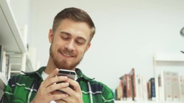 Şık sakallı ve bıyıklı neşeli bir genç adam telefonunda bir mesaj okuyup kahkahaya boğuluyor. Parlak bir kütüphanede, kitaplarla çevrili bir şekilde, kameraya sıcak bir gülümsemeyle bakıyor, neşeyi somutlaştırıyor.