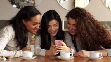 Üç neşeli kız, çekici bir Afrikalı Amerikalı ve sevimli bir Kafkasyalı tarafından çevrelenmiş Asyalı bir kadın şık bir kafede akıllı telefondan komik bir şey izlerken keyifli bir anı paylaşıyorlar. Neşeli ifadeleri ve sıcak atmosferleri...
