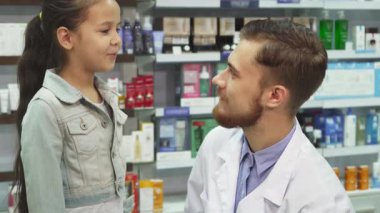 Renkli ürünlerle dolu parlak bir eczanede ilgili bir eczacı ilacı küçük bir kıza nasıl götüreceğini dikkatlice açıklıyor. Sahne, genç kız ve arkadaş canlısı adam arasındaki sıcak bir etkileşimi yakalıyor.