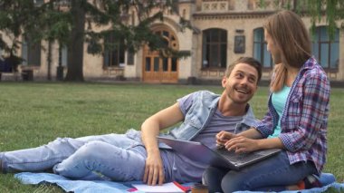 Kafkasyalı birkaç canlı öğrenci üniversite kampüsündeki canlı yeşil çimlerin üzerinde eğlenceli bir çalışma seansına katılıyorlar. Esmer kız, gündelik kıyafetlerle dizlerinin üstüne çöküp dizlerinin üstüne çökerken, erkek arkadaşı, rahatlamış ve gülümsüyor.
