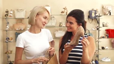 Sevinçli bir esmer göz kamaştırıcı bej bir topuk sergiliyor. Sarışın arkadaşı ise şık bir ayakkabı dükkanında mutluluk saçıyor. Bulaşıcı gülümsemeleri ve enerjik enerjileri moda aşıkları için mükemmel, davetkar bir atmosfer yaratıyor.