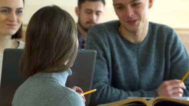 Odaklanmış esmer bir kız öğrenci modern bir konferans salonunda erkek sınıf arkadaşına soru sormak için öne eğiliyor. Çekici beyaz kız, rahat gri bir kazak giyer, defterine yazar yakışıklı oğlan dikkatlice dinler, etrafını sarar.