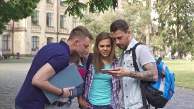 Canlı dört genç öğrenciden oluşan bir grup, iki erkek ve iki kadın, canlı bir kampüsteki akıllı telefon ekranı tarafından büyülenmiş bir şekilde birbirlerine sokuluyorlar. Yakışıklı esmer adam arkadaşlarıyla ilginç bir buluş paylaşırken çekici kızıl saçlı ve...