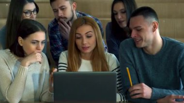 Hem erkek hem de kadın öğrencilerden oluşan çeşitli bir grup modern bir konferans salonundaki dizüstü bilgisayara odaklanmış durumda. Sıcak ahşap tonlar ve hafif ışıklandırmayla çevrili fikirleri tartışırken ifadeleri merak ve işbirliğini yansıtıyor.