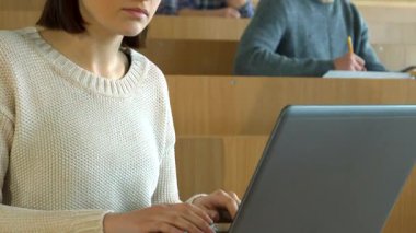 Çekici beyaz bir kız öğrenci, parlak bir konferans salonunda sınıf arkadaşları tarafından çevrelenmiş, dizüstü bilgisayarında daktilo ile derinden meşgul. Sahne, akademik ruhu somutlaştıran öğretim üyesine bakarken onun konsantrasyonunu yakalıyor.