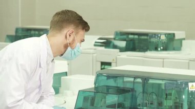 Beyaz laboratuvar önlüğü ve mavi eldiven giymiş kendini işine adamış genç bir laboratuvar teknisyeni kritik analiz için test tüplerini çevirirken laboratuvar santrifüjünü dikkatle izliyor. Onun ciddi ifadesi bu bilimdeki hassasiyetin önemini yansıtıyor.