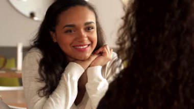 Çekici bir Afrikalı Amerikalı kız, elleri yanağının yanında kıvrılmış, sıcak bir kafede arkadaşına soru soruyor. Sahne, arkadaşlığın sıcaklığını yakalıyor. Yumuşak ışık, onun ışıl ışıl gülüşünü ve davetkar...