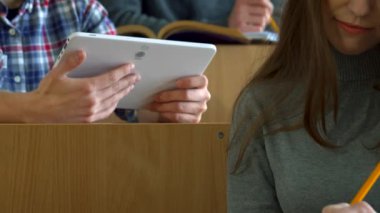 Genç beyaz bir erkek öğrenci heyecanlı bir üniversite konferans salonunda kız sınıf arkadaşına tabletinde ilgi çekici bir şey gösteriyor. Sahne, iş birliğinin ve merakın özünü yakalıyor. Öğrenci arkadaşlarıyla birlikte.