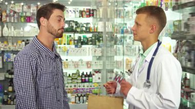 Parlak ve davetkar bir eczanede, dost canlısı bir doktor minnettar bir hastaya her ikisi de gülümseyerek bir paket hap verir. Sahne, bir anlık bakım ve profesyonelliği yakalıyor, eczacılık ürünlerinin canlı dizilimini gözler önüne seriyor.