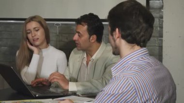 Çekici, genç, sakallı bir iş adamı, meslektaşlarıyla canlı bir tartışmaya girerken omuzlarının üzerinden sıcak bir gülümseme sergiliyor. Atmosfer, canlı bir ofis ortamı sergileyen pozitiflik ve işbirliğiyle yükleniyor.