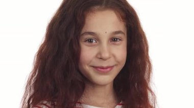 Hoş küçük bir kız saf beyaz bir arka plana karşı duruyor, kıvırcık siyah saçları neşeli yüzünü çerçeveliyor. Bulaşıcı gülüşü ve tatlı gülüşü sevinç ve sıcaklığı çağrıştırıyor. Bayram sezonunu kutlamak için mükemmel.