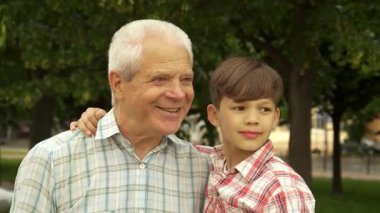 Büyüleyici küçük bir çocuk büyükbabasının kulağına bir sır fısıldamak için eğiliyor ve dışarıda iç açıcı bir an yaratıyor. Çekici esmer çocuk, neşeli bir şapka takıyor ve yakışıklı büyükbabasıyla neşeli bir bağ kuruyor.