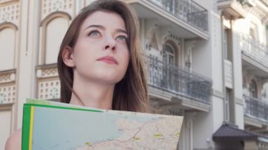 Neşeli bir kadın elinde renkli bir harita tutarken kameraya ışıldıyor, şehir ortamında macera ruhunu somutlaştırıyor. Hareketli gülüşü ve arka plandaki büyüleyici mimarisi herkesi kendisine katılmaya davet eden canlı bir atmosfer yaratıyor.